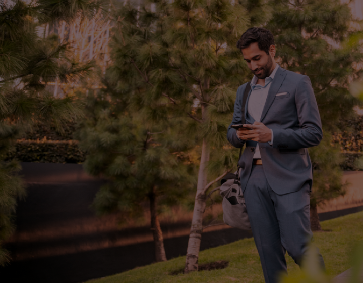 Man dressed in business suit walking on wooded path reading phone