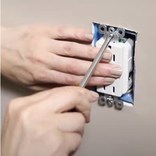 Installer fastening outlet to the wall box using a screwdriver